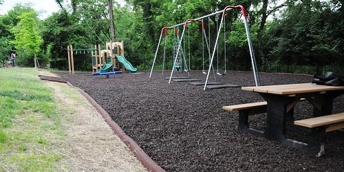 Children's playground with swings and a slide beside the woods